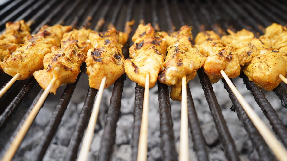 Brochettes de poulet en train de griller sur une plancha en fonte